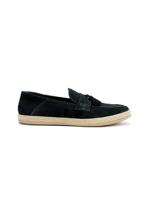 Zapato negro de ante tipo slip-on con suela plana de yute trenzado y un tassel decorativo en la parte delantera, que cuenta con una punta redondeada y costuras mínimas.