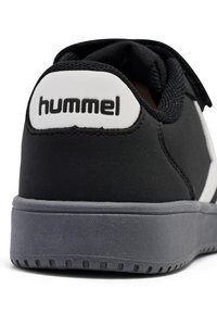 Svart sneaker i syntetmateriale, med en vit logotyp på hälen, grå sula och texturerad yta. Accenterad av en slank design.
