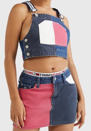 Mujer que lleva un top corto y minifalda vaqueros bicolor con parches en rosa, azul y blanco, con una cintura elástica con la marca Tommy Jeans.