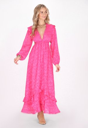 Langes rosa Blümchenkleid mit langen Ärmeln, tiefem V-Ausschnitt, gerafftem Saum und fließender Silhouette; kombiniert mit beigen Knöchelstiefeln.