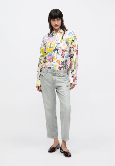 Chemise boutonnée avec des imprimés graphiques colorés et variés sur fond blanc, associée à un jean droit gris clair et des ballerines noires.