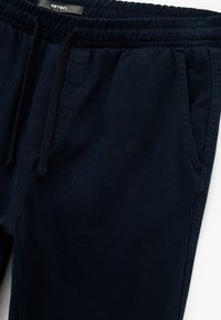 Marineblå joggebukser lavet af bomuld. Har en elastisk talje med snor, sidelommer og en glat overflade.