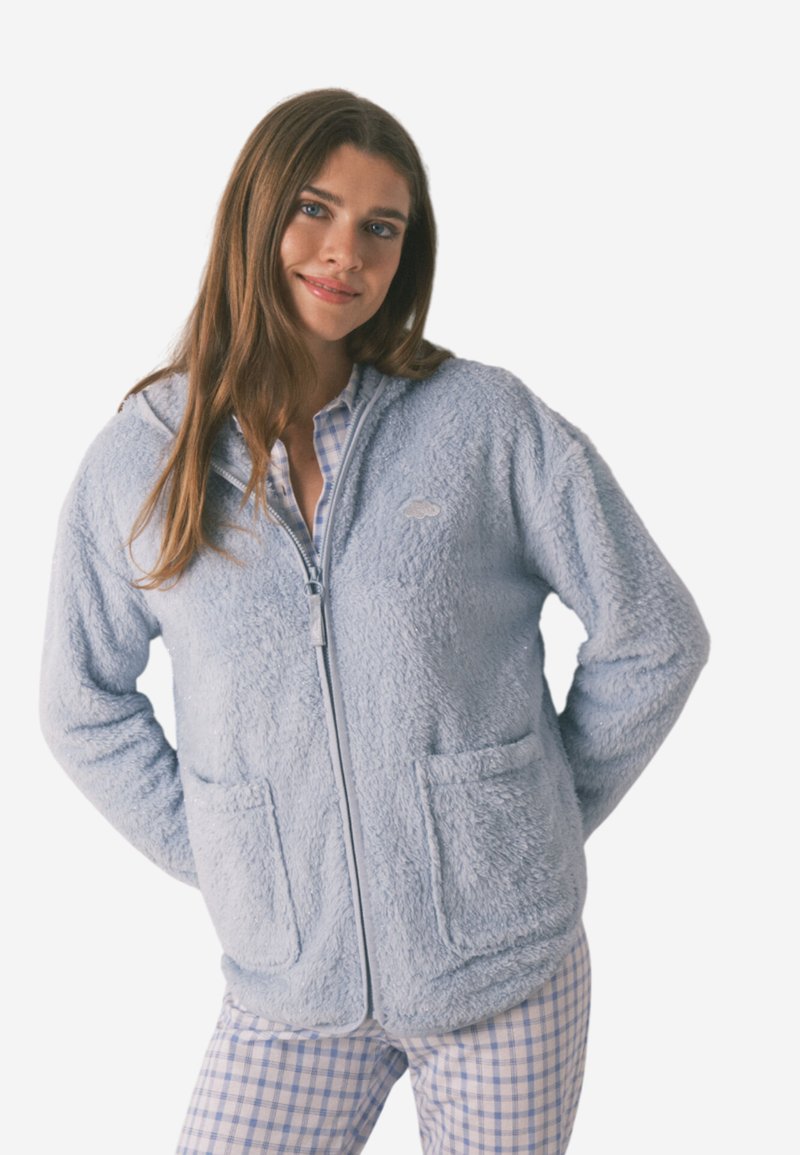 Helles, flauschiges, zip-fähiges Kapuzenoberteil in Blau mit zwei Vorder taschen und einem kleinen Logo. Trägt man über einem karierten Schlafanzugshirt, das eine weiche Textur aufweist.