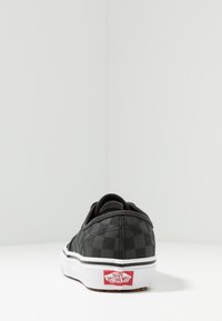 Czarno-biała szachownica na płóciennych klapach z białą gumową podeszwą, z czerwonym logo "Vans Off The Wall" na pięcie.