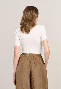 White fitted t-shirt with short sleeves, paired with loose, brown, wrinkled trousers featuring an elastic waistband.