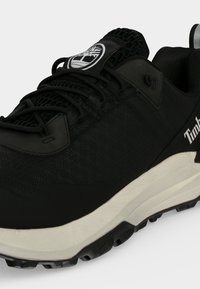 Μαύρο αθλητικό παπούτσι Timberland με επάνω μέρος από δίχτυ, μαύρα κορδόνια, λευκή ενδιάμεση σόλα και λογότυπο της μάρκας στη γλώσσα και στην πλευρά.