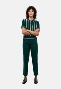 Polo-shirt à rayures vertes avec patte de boutonnage, associé à un pantalon vert assorti. La tenue présente une coupe décontractée et des chaussures plates.