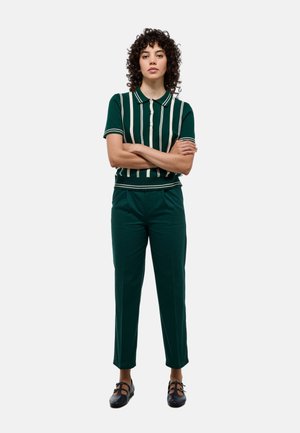 Polo-shirt à rayures vertes avec patte de boutonnage, associé à un pantalon vert assorti. La tenue présente une coupe décontractée et des chaussures plates.