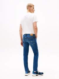 Blå denimjeans med slim fit, som har en baklomme og subtil søm. Kombinert med en hvit t-skjorte og blå sneakers.