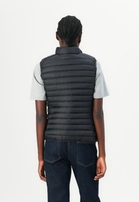 Black puffer vest with horizontal quilted design. Features a high collar and is worn over a gray t-shirt. Back view shows subtle sheen.