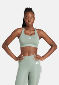 Reggiseno sportivo verde chiaro con una texture liscia, caratterizzato da una fascia di larghezza media e un logo con tre strisce bianche sul davanti.