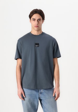 Gray cotton t-shirt with a round neckline and short sleeves, featuring a small black logo patch on the front. Classic fit with a smooth texture.