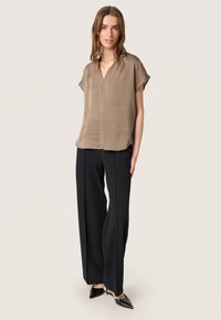 Blouse courte en tissu texturé marron avec un col en V, assortie à un pantalon large noir et des escarpins noirs à bout pointu. Design simple, couleurs neutres.