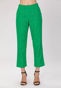 Pantalons verts coupés en tissu texturé avec des motifs découpés. Dotés d'une taille haute et associés à des sandales noires à lanières.