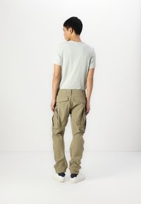 Lys grønn t-skjorte med korte ermer og khaki cargo bukser med flere sidelommer, kombinert med hvite sneakers, sett fra baksiden.