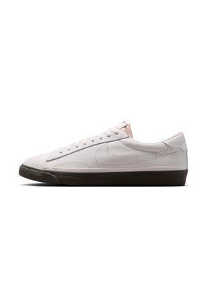 Niski biały sneaker z perforowanym logo po boku, białymi sznurowadłami i grubą czarną gumową podeszwą, pokazany z profilu na białym tle.