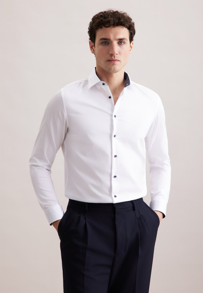 Witte button-up shirt met contrasterende patroon kraag, lange mouwen en marineblauwe knopen, gecombineerd met donkere broeken. Gladde stoftextuur.