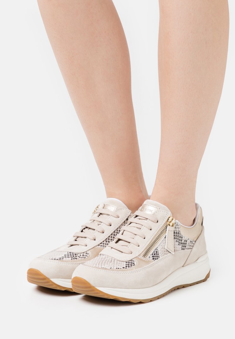 Baskets beiges avec un imprimé reptile, des lacets, une fermeture éclair latérale et une semelle en caoutchouc brun clair avec un profil coussiné.