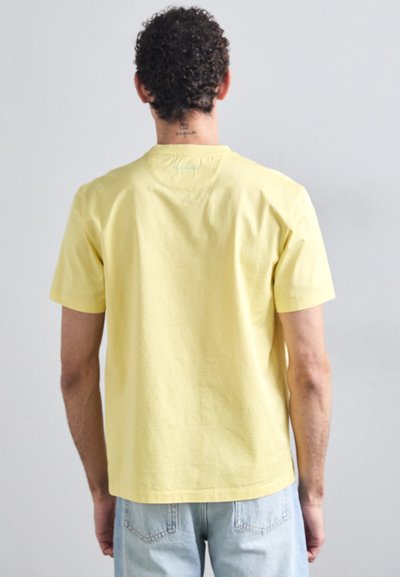 Yellow cotton t-shirt with short sleeves, round neck, and a soft texture. Back features a small green accent near the collar.