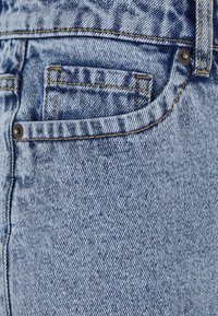 Světle modré džíny z denimu s texturovaným povrchem, s viditelným švem, boční kapsou a kovovým knoflíkem jako ozdobou.