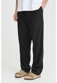 Black relaxed-fit trousers made of lightweight fabric, featuring side pockets, paired with beige sandals with a foot strap design.