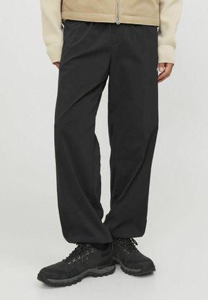 Pantalons noirs amples en tissu léger ; dotés d'une taille élastique et de poches latérales, associés à des baskets noires.