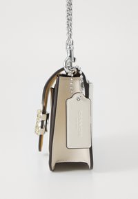 Brown leather handbag with silver chain strap, featuring a jeweled clasp and a beige interior. Includes a tag with "COACH" branding.