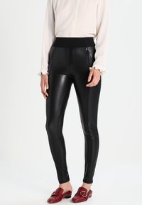 Leggings en simili cuir noir avec une taille élastique haute, dotés de poches latérales zippées et d'une texture lisse et brillante.