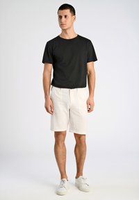 T-shirt nera in cotone a maniche corte, abbinata a pantaloni corti a coste color crema con tasche laterali e sneakers bianche.