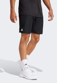 Black athletic shorts made of lightweight fabric, featuring a white three-stripe logo. Paired with white shoes and socks.