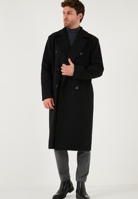 Melnas vilnas maisījuma divrindas mēteles ar lielām atlokām, sānu kabatām un melniem pogām, savienotas ar pelēku augsto apkakli un biksēm.