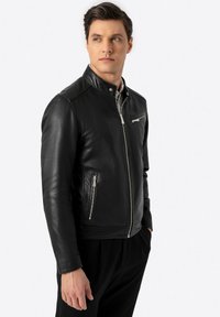 Schwarze Lederjacke mit Stehkragen, Reißverschlusstaschen und dezenten Steppnähten. Das Design weist eine schlanke und taillierte Form auf.