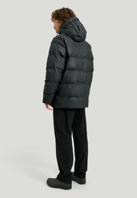 Mustahuk black puffer takki with baal, yranottar quilted design and matte finish, in paired mitt black trousers and dark footwear.