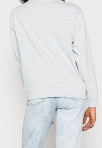 Sweatshirt gris avec une coupe décontractée, un col rond et des poignets côtelés, associé à un jean en denim décoloré et légèrement lavé.