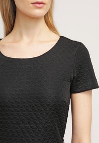 Svart texturerad blus med diamantmönster, korta ärmar och rund halsringning, tillverkad av vävt tyg.