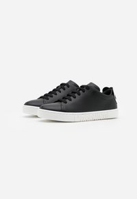 Paire de baskets en cuir noir avec lacets noirs et semelles blanches embossées du mot "MOSCHINO" sur un fond blanc uni.