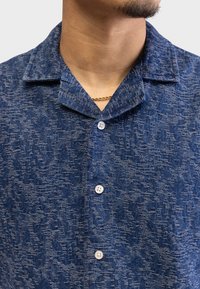 Short-sleeved blue collared shirt with a textured fabric, featuring a subtle pattern and white buttons on the front placket.
