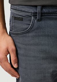 Jeans in denim grigio scuro con un design aderente; presentano una tasca frontale e un piccolo tag logo nero vicino alla vita.