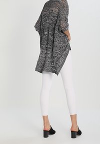 Svart och vit genomskinlig cardigan med lös passform och korta ärmar, i kombination med vita smala jeans och svarta öppna tofflor.