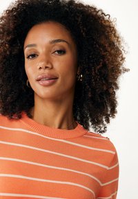 Pomarańczowy sweter z prążkowanym kołnierzem i guzikami na ramionach. Materiał wydaje się gładki o lekkiej strukturze.