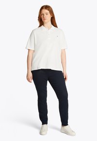 White short-sleeve polo shirt with a three-button placket. Paired with dark navy slim-fit pants and white sneakers. Simple, casual design.