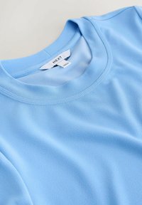 T-shirt bleu clair à col rond avec texture de tissu lisse et coutures visibles autour de l'encolure et des épaules, étiqueté "NEXT".