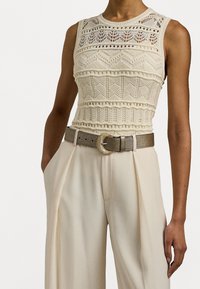 Ärmlös krämfärgad virkade topp tillsammans med högmidjade vida krämfärgade byxor och ett metalliskt bälte med en rund spänne.