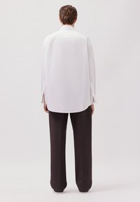 Camicia bianca con bottoni e maniche lunghe, con spacchi laterali, abbinata a pantaloni neri larghi. Texture del tessuto liscia; design semplice.