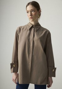 Brown collared shirt with long sleeves and button cuffs featuring star-shaped accents. Smooth texture, relaxed fit, and straight hem.
