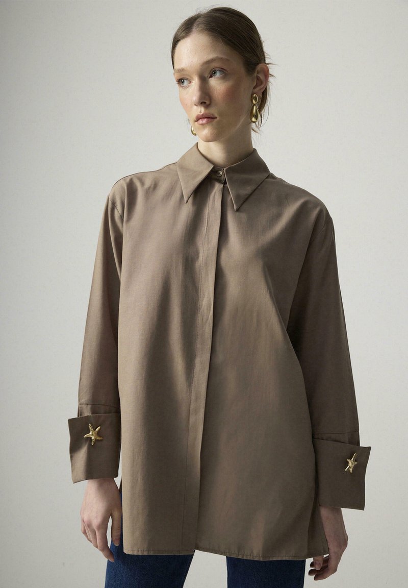 Brown collared shirt with long sleeves and button cuffs featuring star-shaped accents. Smooth texture, relaxed fit, and straight hem.