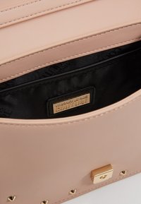 Light pink leather handbag with a gold clasp, featuring a textured surface, pin stud accents, and a black interior with a logo label.
