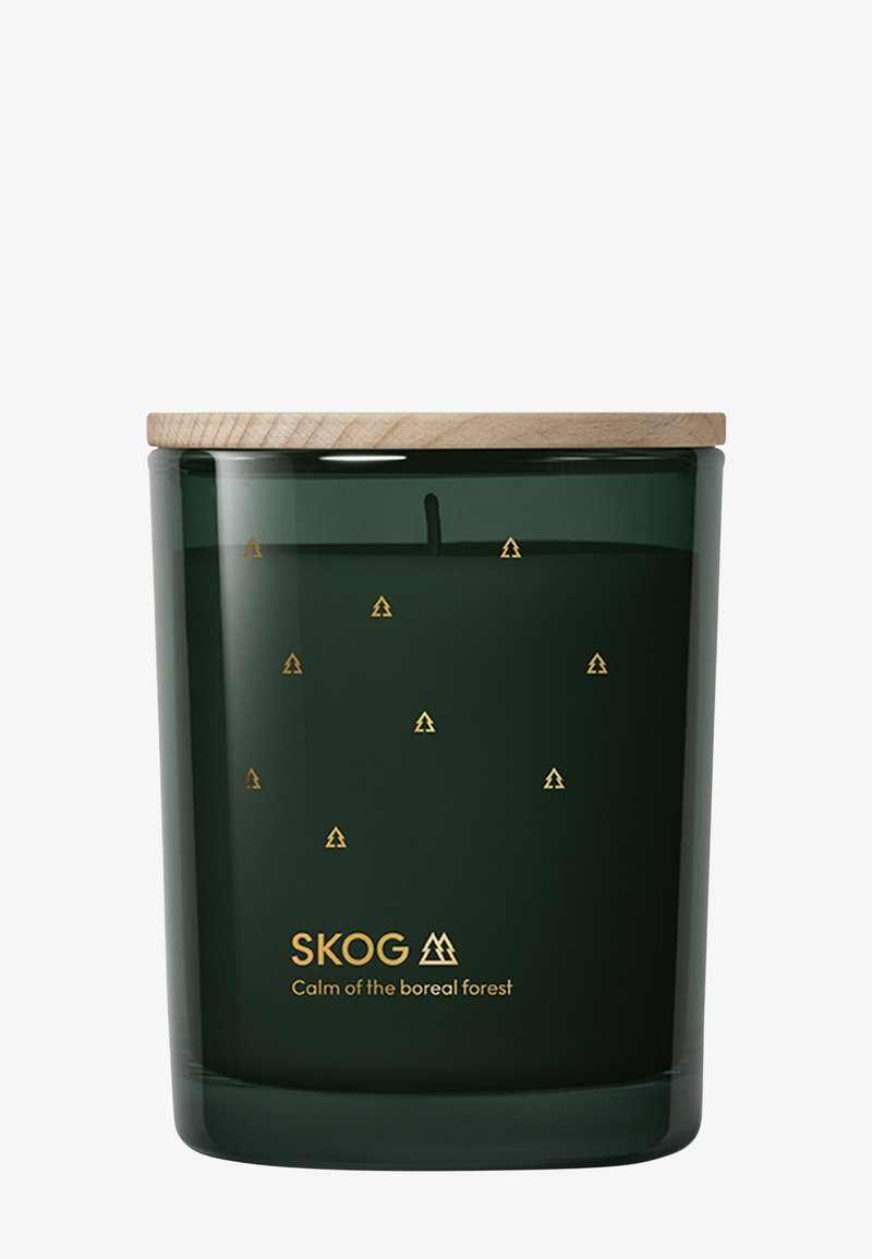Mörkgrön glasljus med trälock, små gyllene trädkonstikoner och texten "SKOG Lugnet i den boreala skogen" på framsidan.