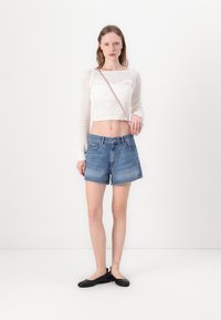 Top corto de punto blanco con mangas largas, pantalones cortos de mezclilla azul claro y mocasines negros. Diseño simple, textura ligera y ajuste casual.
