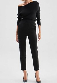 Pull noir côtelé à col bardot avec manches longues, associé à un pantalon noir ajusté. Les tenues sont complétées par des escarpins noirs à bout pointu.